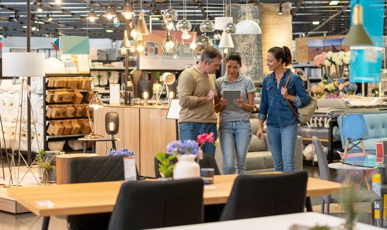 A man and woman walking around a furniture store and looking at a tablet held out by a saleswoman.