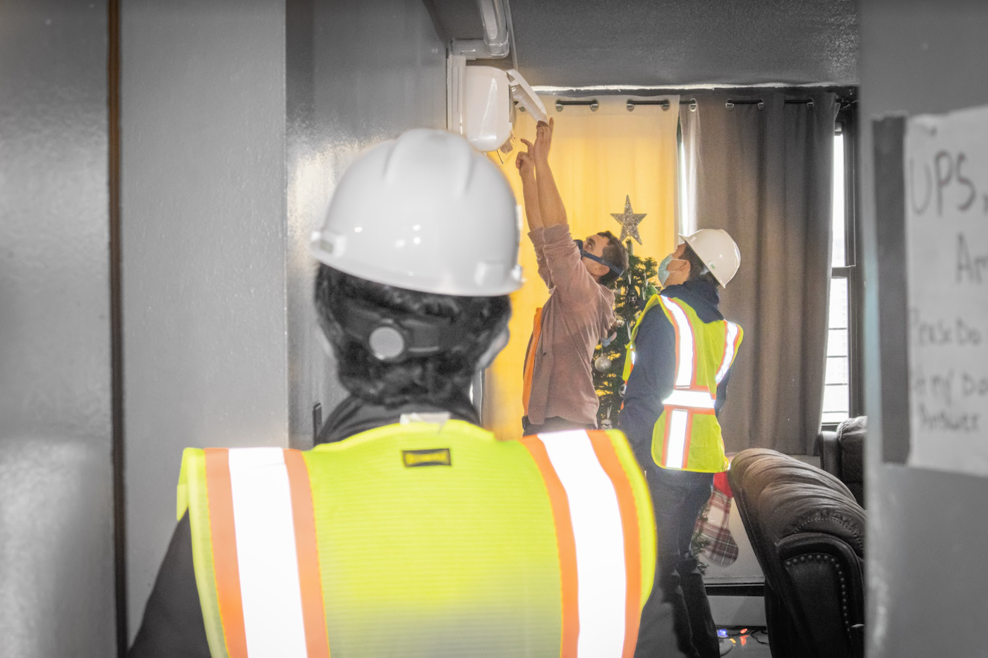Workers in neon vests install a heat pump on the wall of an apartment